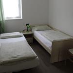 Zwei Einzelbetten, Nachttisch mit Lampe, Stuhl und Fenster.