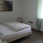 Schlafzimmer mit Bett, Stuhl und Fenster mit grünen Vorhängen.