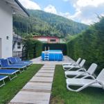 Hinterhof mit Pool, Liegen und grünem Garten. Berglandschaft im Hintergrund.