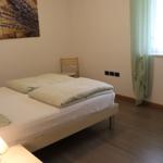 Schlafzimmer mit Bett, Wandbild, Stuhl und Fenster mit Vorhängen.