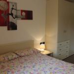 Schlafzimmer mit Bett, Nachttisch und Kleiderschrank. Wandbild mit Tanzfiguren.