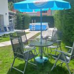 Gartenbereich mit Liegen, Pool und Tisch mit Stühlen unter einem blauen Sonnenschirm.