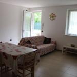 Wohn- und Essbereich mit Tisch, Stühlen und Sofa. Fenster und Glastür mit Blick nach draußen.