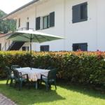 Terrasse mit Tisch, Stühlen und Sonnenschirm vor weißem Haus mit Hecke.