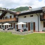 Wohnhaus mit Balkonen, Garten und Sonnenschirmen. Berglandschaft im Hintergrund.