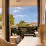 Sliding glass doors open to a terrace with seating and view of trees and buildings.