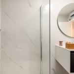 Bathroom with shower, sink, and round mirror.