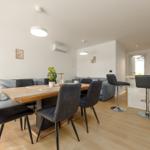 Dining area with wooden table and chairs, sofa, and kitchen counter in background.
