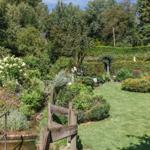 Garten mit grünem Rasen, Blumenbeeten und Holzbrücke über einen kleinen Teich.