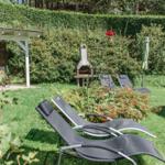 Garten mit Liegestühlen, Grill und Pavillon. Grünflächen und Hecke im Hintergrund.