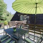 Terrasse mit Tisch, Stühlen und grünem Sonnenschirm. Hintergrund: Holzgeländer und Haus.