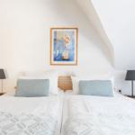 Zwei Betten unter einem Dachschrägen mit Nachttischen und Wandbild.