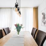 Esszimmer mit langer Tischplatte, Stühlen und Blumenarrangement.