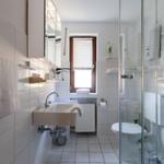 Badezimmer mit Dusche, Waschbecken und Toilette. Fenster mit Jalousie.