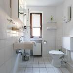 Badezimmer mit Toilette, Waschbecken und Dusche. Fenster mit Jalousie.