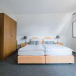 Zimmer mit Doppelbett, Holzschrank und Fenster mit Vorhängen.