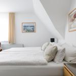 Schlafzimmer mit Doppelbett, Wandbildern und Holzmöbeln unter schrägen Dachschrägen.