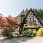 Fachwerkhaus mit Balkon, umgeben von Bäumen und Sträuchern.