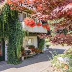 Haus mit Kletterpflanzen, Blumenkästen und Balkon unter roten Blättern.