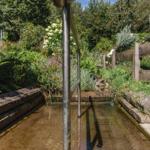 Ein kleiner Bach fließt durch einen grünen Garten mit Steinufer und Holzgeländer.