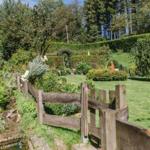 Garten mit Holzgeländer, Blumenbeeten und grünem Rasenhang