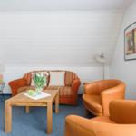 Wohnzimmer mit Sofa, zwei Sesseln und Tisch. An der Wand hängt ein Bild.