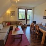 Living and dining area with sofa, table, and chairs. Window with view of balcony and forest.