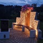 Garden area with stone bench, flower box, and lighting at dusk.
