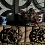 Two blue ceramic pots, a basket with red flowers, and two wooden wheels on stone wall.