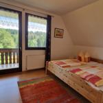 Bedroom with balcony, wooden bed, and wardrobe. View of forest.