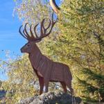 Wooden sculpture of a deer on a rock in the forest with autumn leaves.