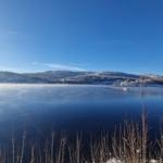 Snow-covered hills surround a calm lake with a small boat.