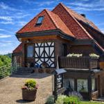Holiday home with red tiled roof, wooden balcony, and flower beds in greenery.