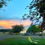 Zwei grüne Liegestühle vor einem Bauernhof bei Sonnenuntergang.