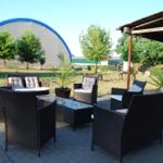 Terrasse mit Sitzgruppe, Grill und Holzstapel im Hintergrund.