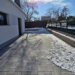 Pflasterter Weg neben Haus mit Schnee und Bäumen im Hintergrund.