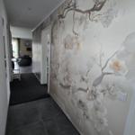 Flur mit floraler Wandtapete und dunklem Bodenbelag. Blick in Wohnbereich mit Sitzmöbeln.