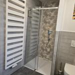 Dusche mit Glaswand, Heizkörper und Toilette in moderner Ausstattung.