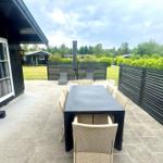 Terrace with table, chairs, and loungers. Black wooden fences and green garden.