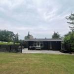 Black cabin with terrace, grill, and garden. Surrounded by trees and shrubs.