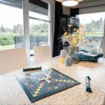Dining table with Scrabble game, flowers and mugs by windows overlooking garden.