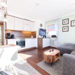 Wohnküche mit Essbereich, Sofa und Fernseher. Holzboden und hell gestrichene Wände.