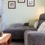 Ein Wohnzimmer mit grauem Sofa, Holztisch und Fenster mit Vorhängen.