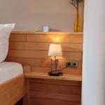 Hölzernes Bett mit Nachttisch, Lampe und Vase an der Wand