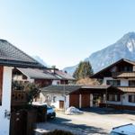 Haus mit Balkon und Bergblick. Parkplatz und Schneehaufen sichtbar.