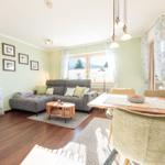 Wohn- und Essbereich mit Sofa, Tisch und Stühlen. Fenster mit Vorhängen und Wandbilder.