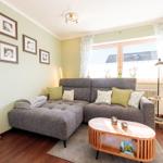 Wohnzimmer mit grauem Sofa, Holztisch und Fenster mit Vorhängen.