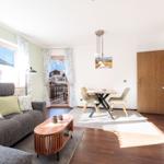 Wohn- und Essbereich mit Sofa, Tisch, Küchenzeile und Balkontür.