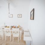 Esszimmer mit weißem Tisch und Stühlen, Wandbildern und Bänkchen mit Kissen.