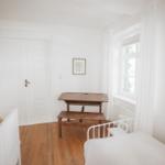 Zimmer mit Holzboden, weißer Tür, Tisch und Bett.